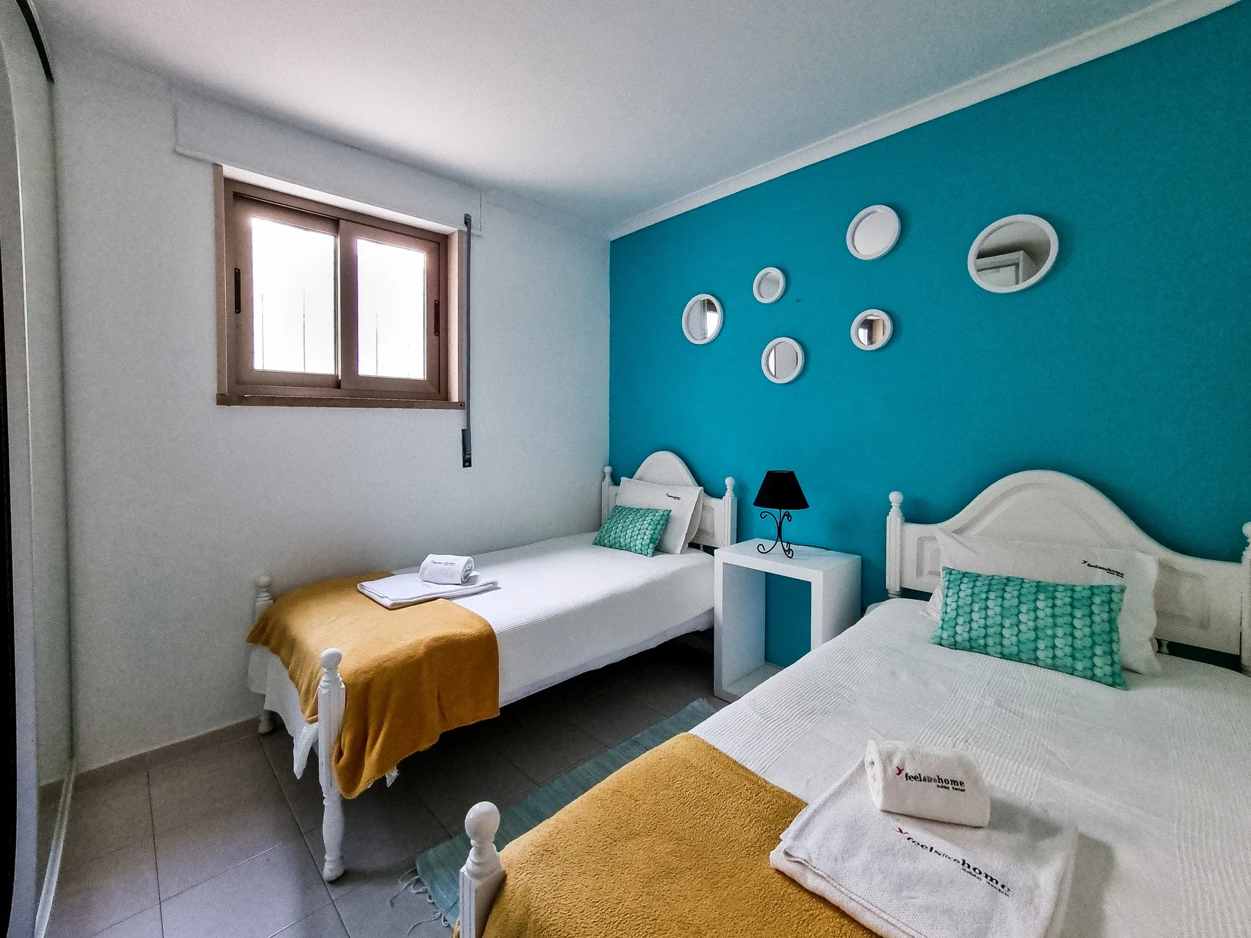 A bedroom with two beds, turquoise accents, and small round wall mirrors.