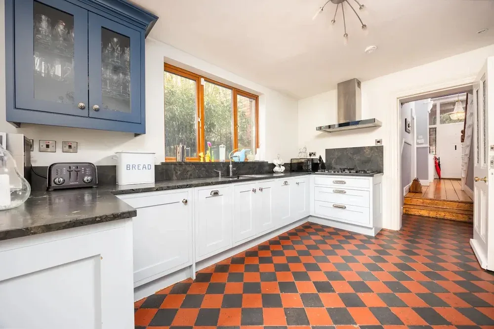A bright kitchen with white cabinets, dark countertops, and a checkerboard floor.