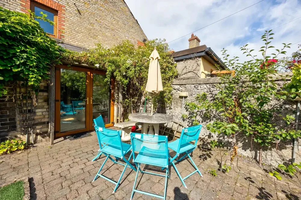 A paved outdoor patio with turquoise seating, a table, and surrounding greenery.
