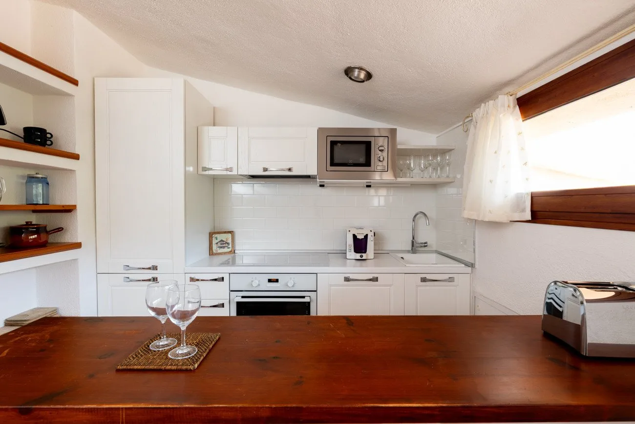 A compact white kitchen with a microwave, sink, and wooden dining table.