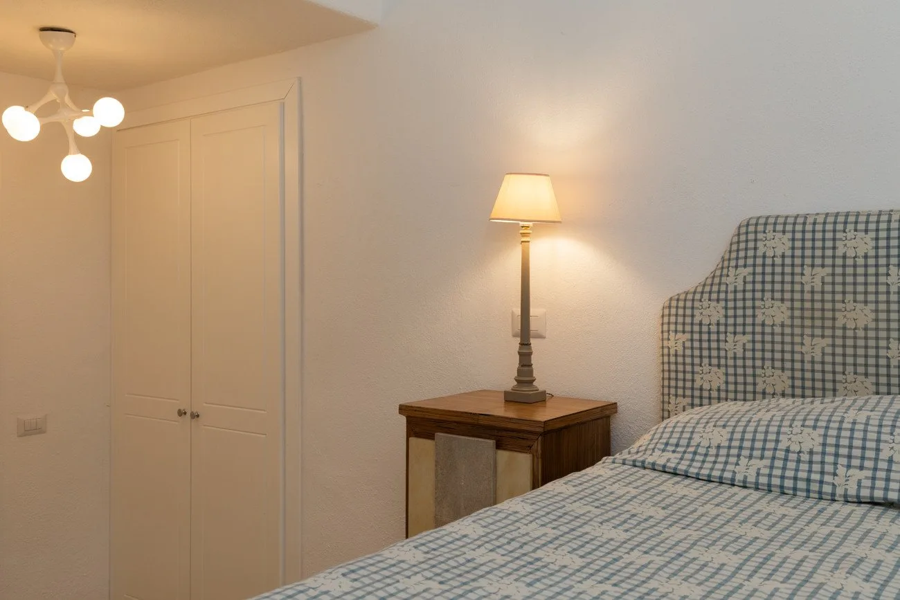A bedroom with patterned bedding and a bedside table topped by a lamp.