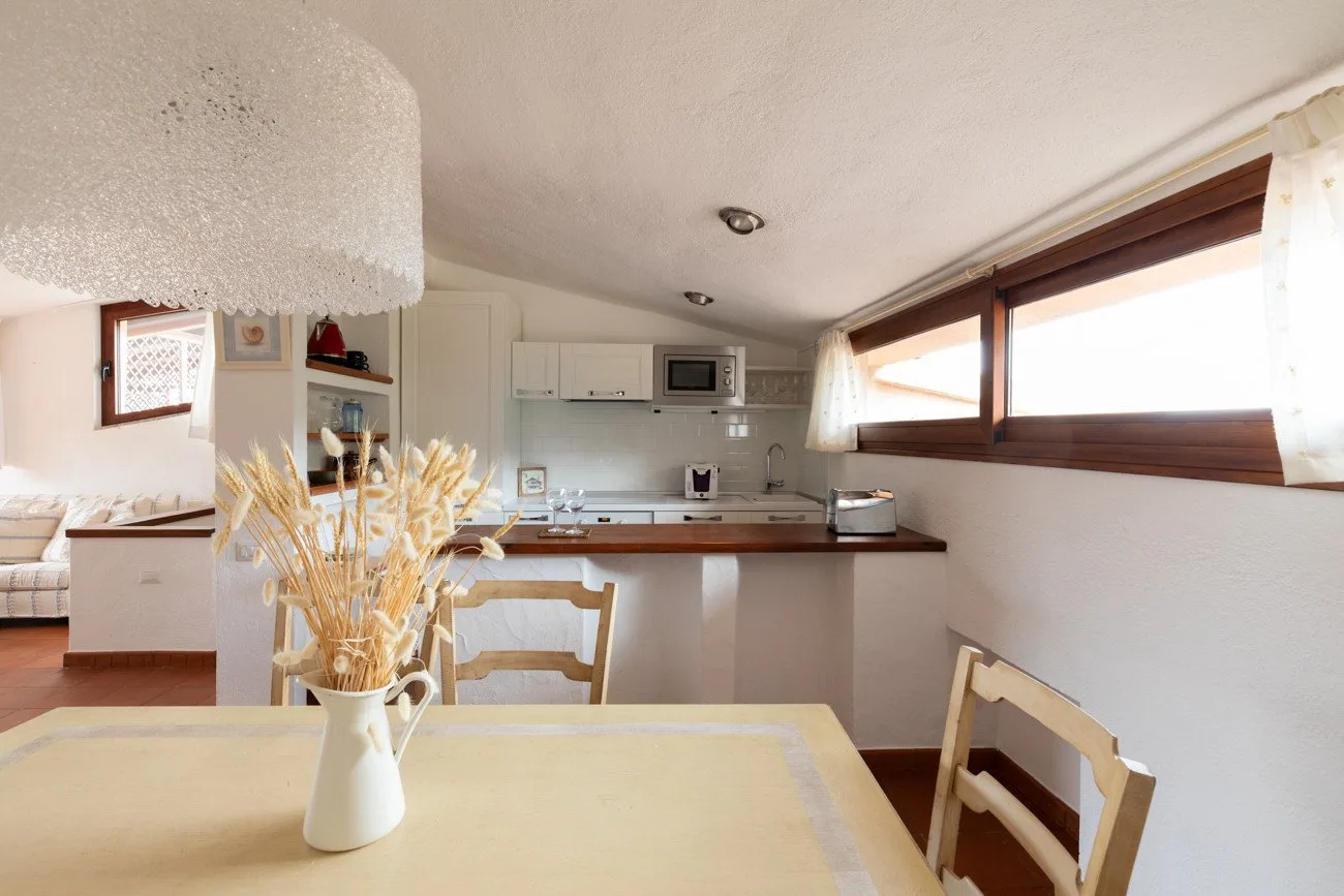 A dining area opens onto a kitchen, with a table in the foreground.