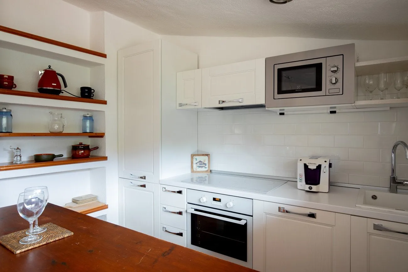 A bright kitchen with white cabinets, a built-in oven, and open shelves.