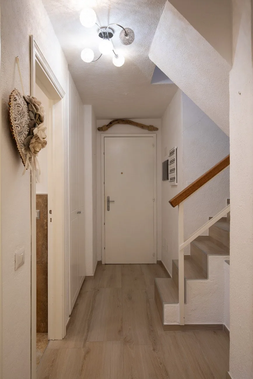 A narrow hallway with a closed door and a staircase along one side.