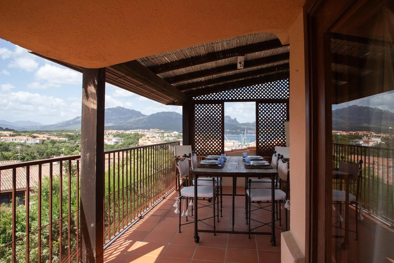 A covered outdoor dining area overlooks a hillside town and distant mountains.