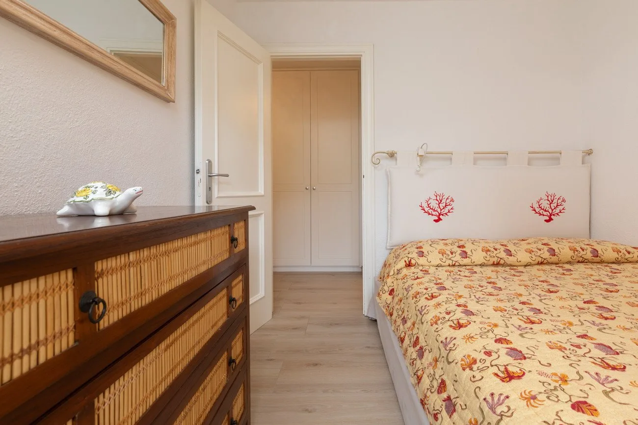 A bedroom with a floral bedspread and a wooden dresser.