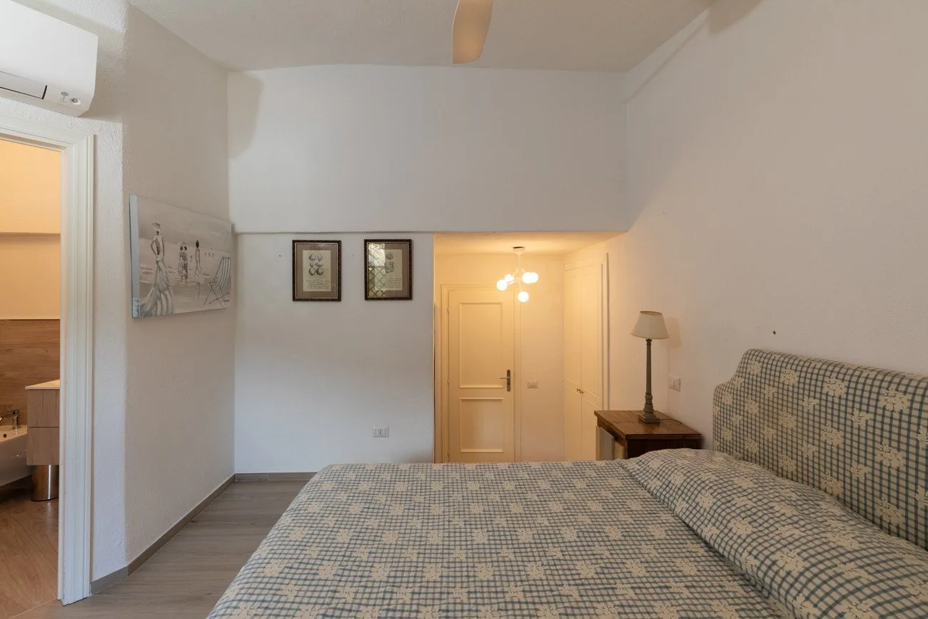 A bedroom with a patterned bedspread and a lit doorway.