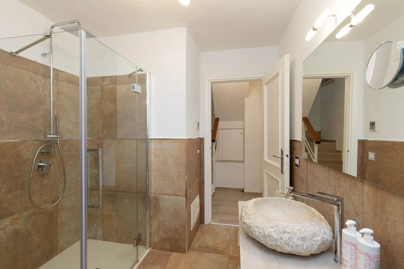 A bathroom with a glass shower, stone sink, and wall mirror.