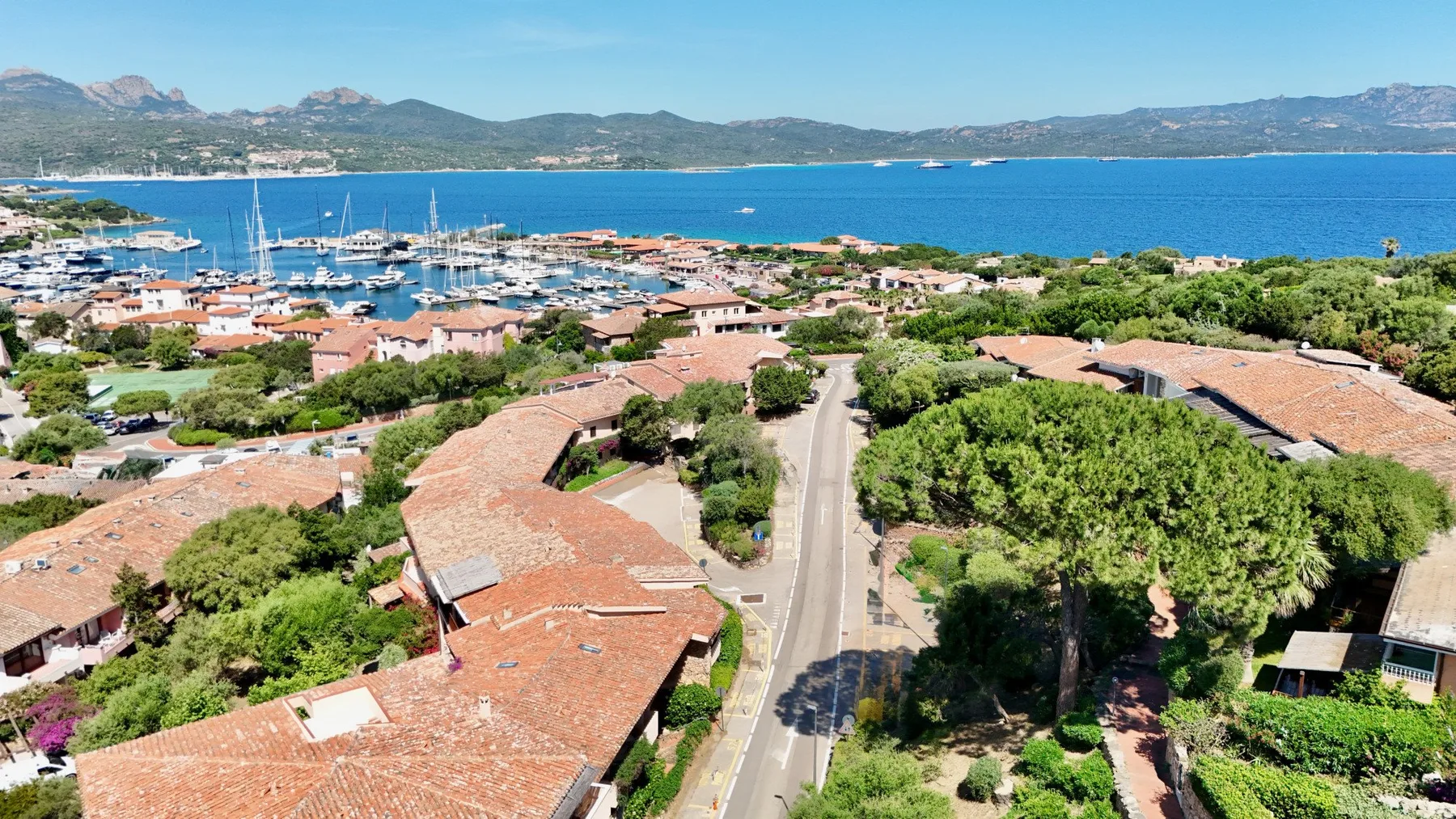 An aerial view of a coastal town, with a road leading toward the harbor and blue sea.