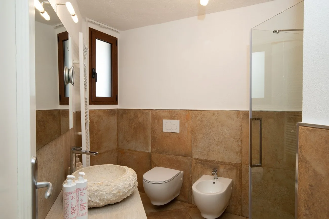 A bathroom with a sink, toilet, bidet, and glass shower.