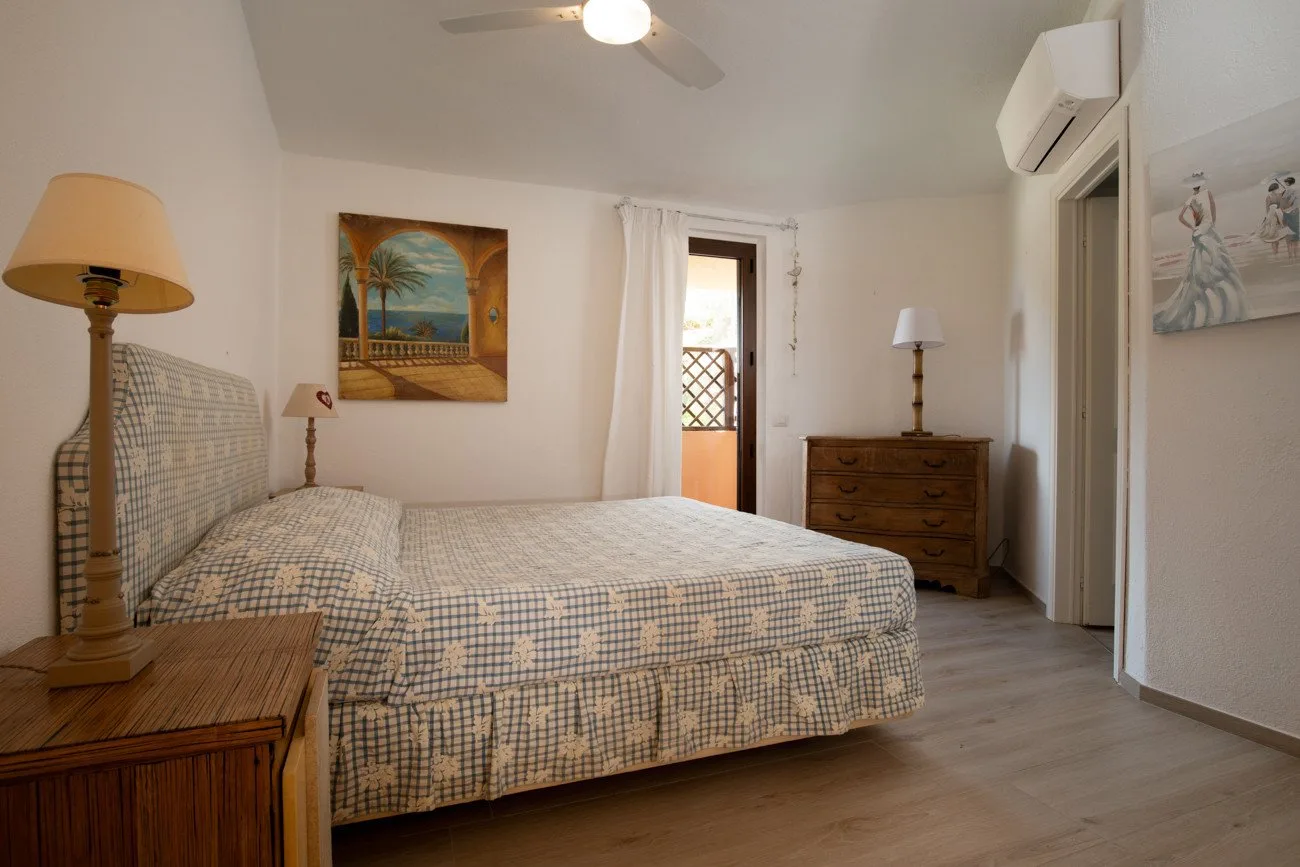 A bedroom with a patterned bed, bedside furniture, and a doorway opening to a balcony.