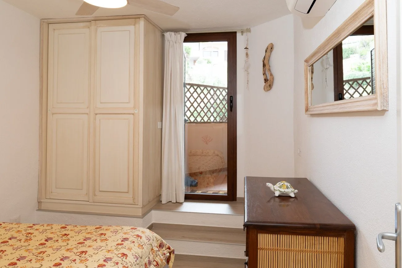 A bedroom with a bed, a wooden wardrobe, and a window overlooking a balcony.