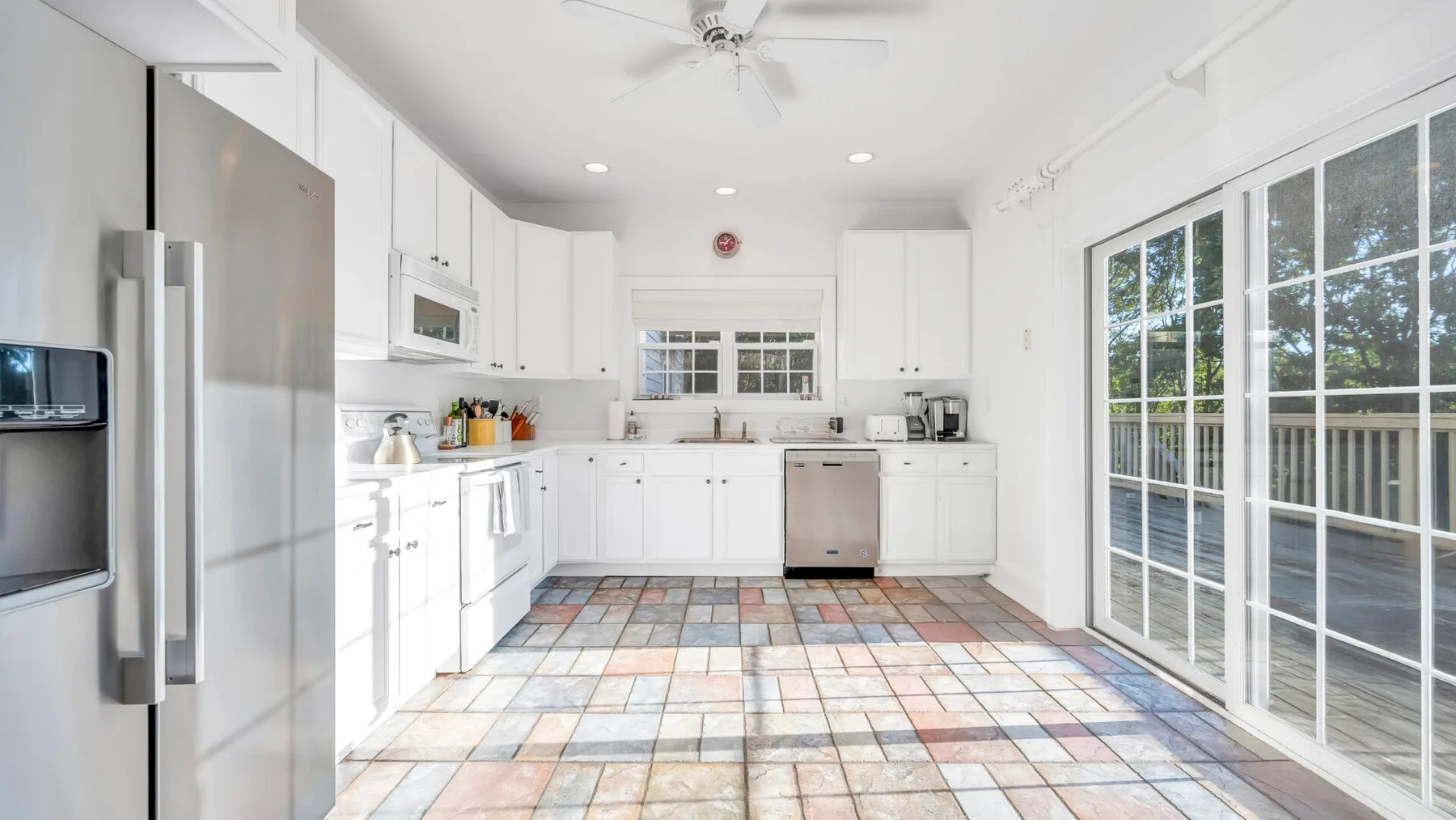 Una cocina luminosa con gabinetes blancos y grandes puertas de vidrio hacia el exterior.