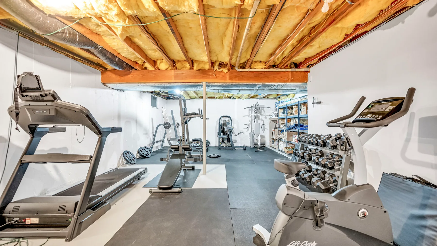 Un gimnasio en el sótano con cintas de correr, máquinas de pesas y mancuernas.