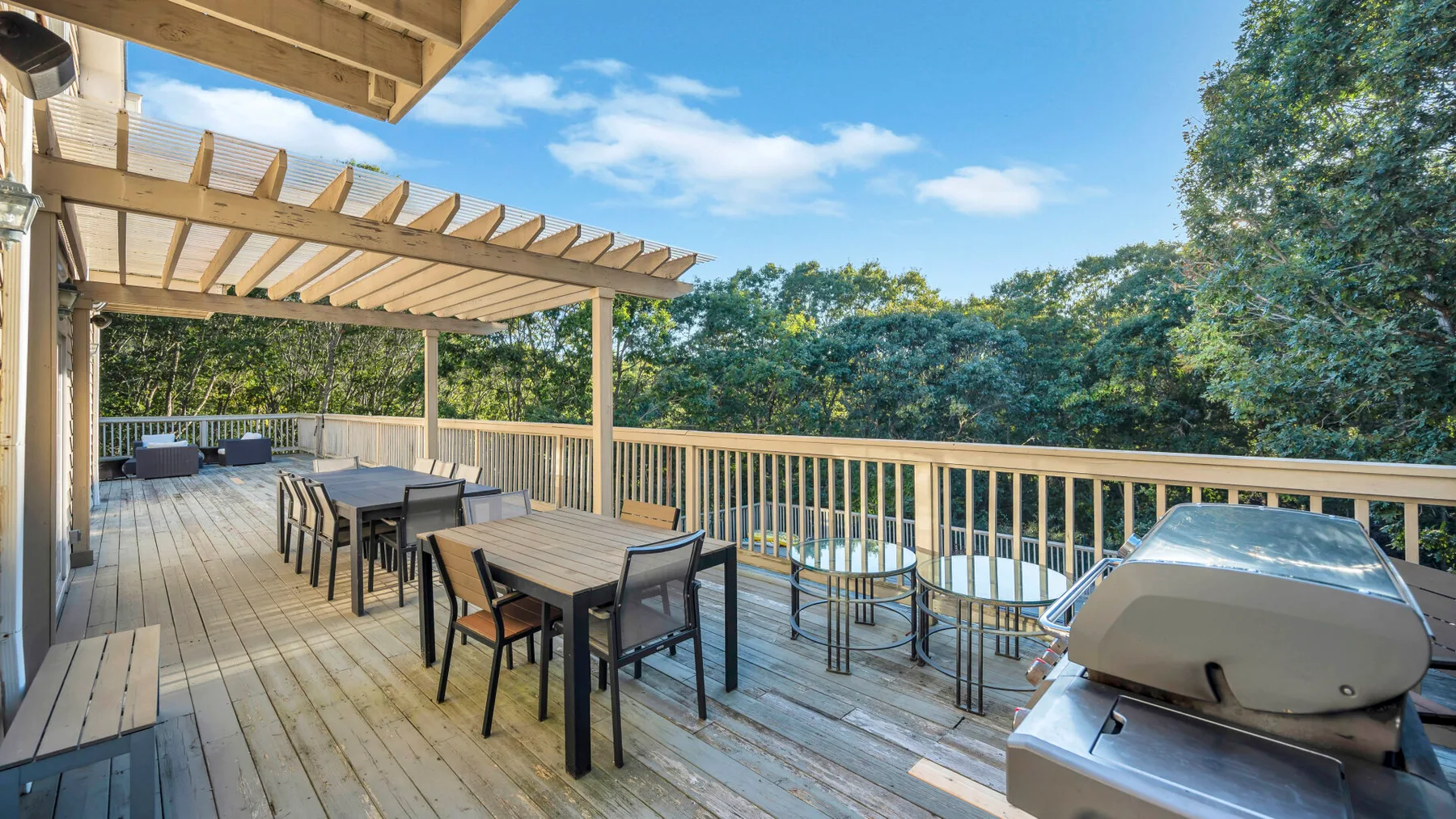 Una terraza exterior de madera tiene mesas, asientos y una parrilla.