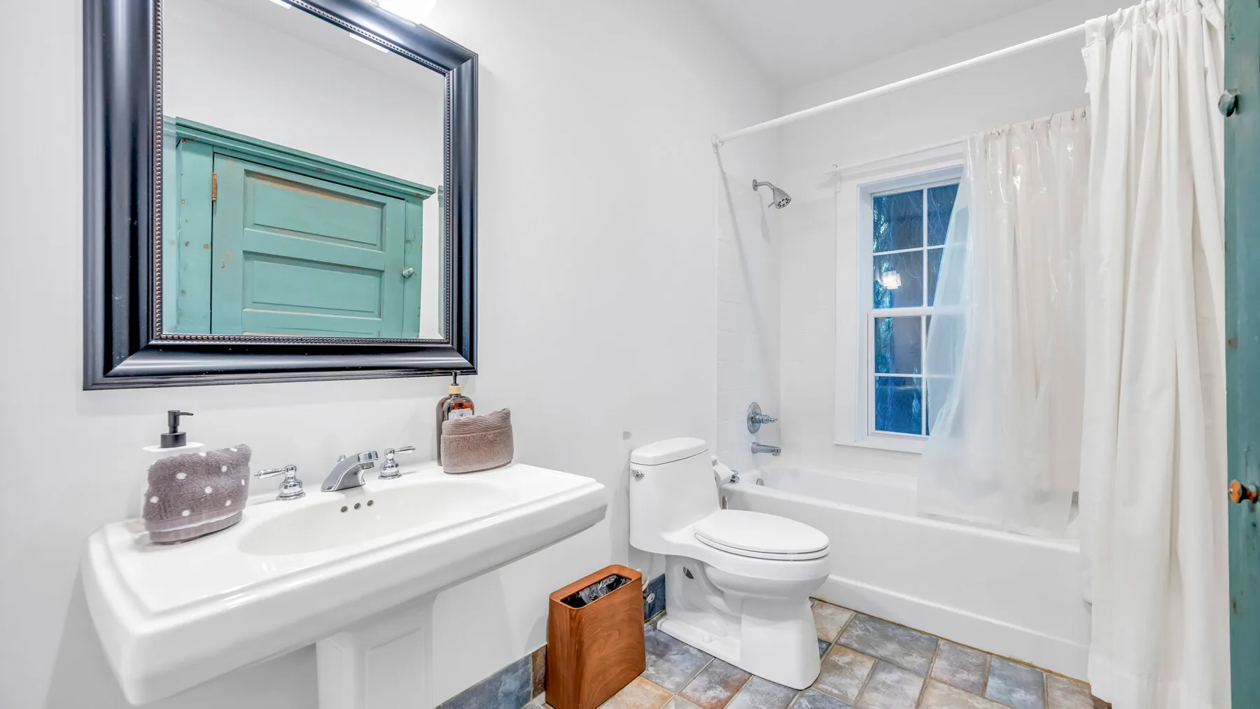 Baño con lavabo, inodoro y bañera junto a una ventana con cortina.