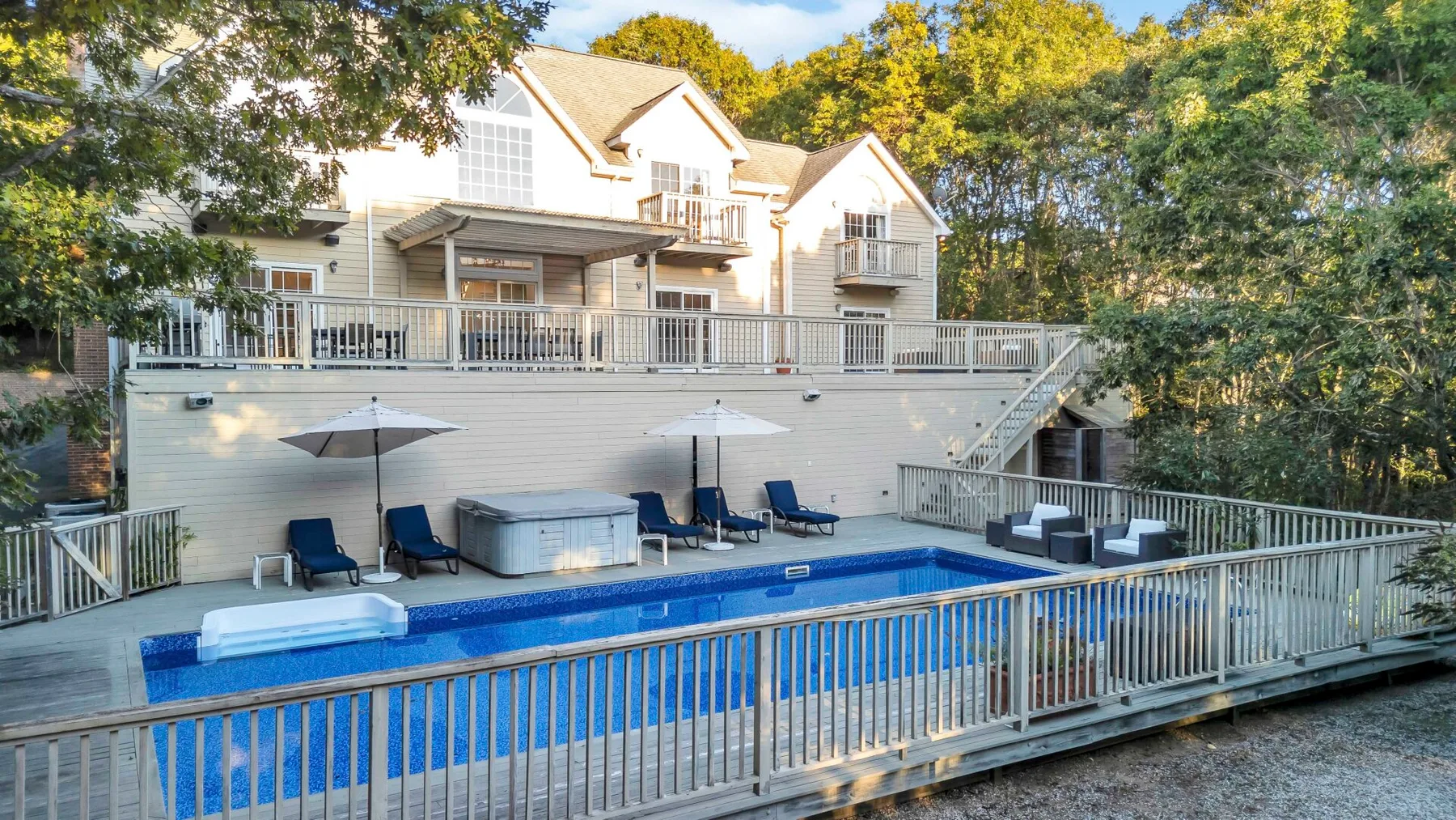 Una piscina está junto a una casa grande, rodeada de árboles.