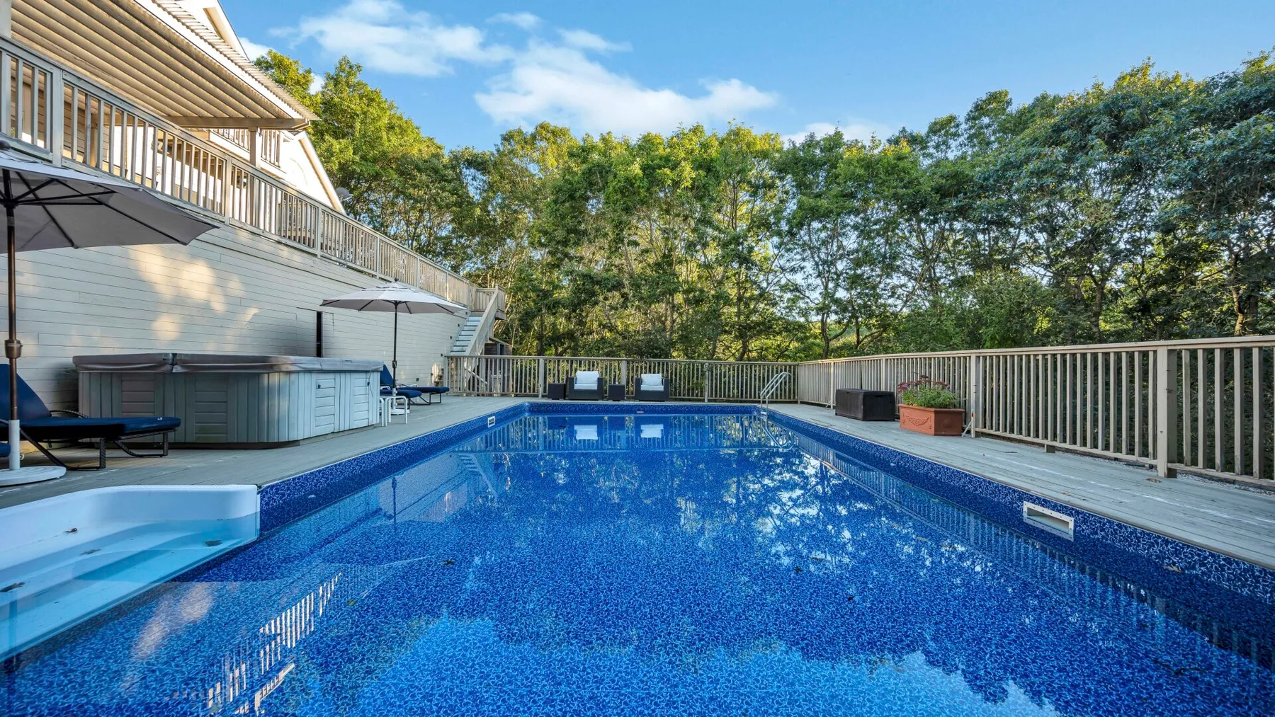 Una piscina al aire libre está junto a una terraza de madera y árboles frondosos.