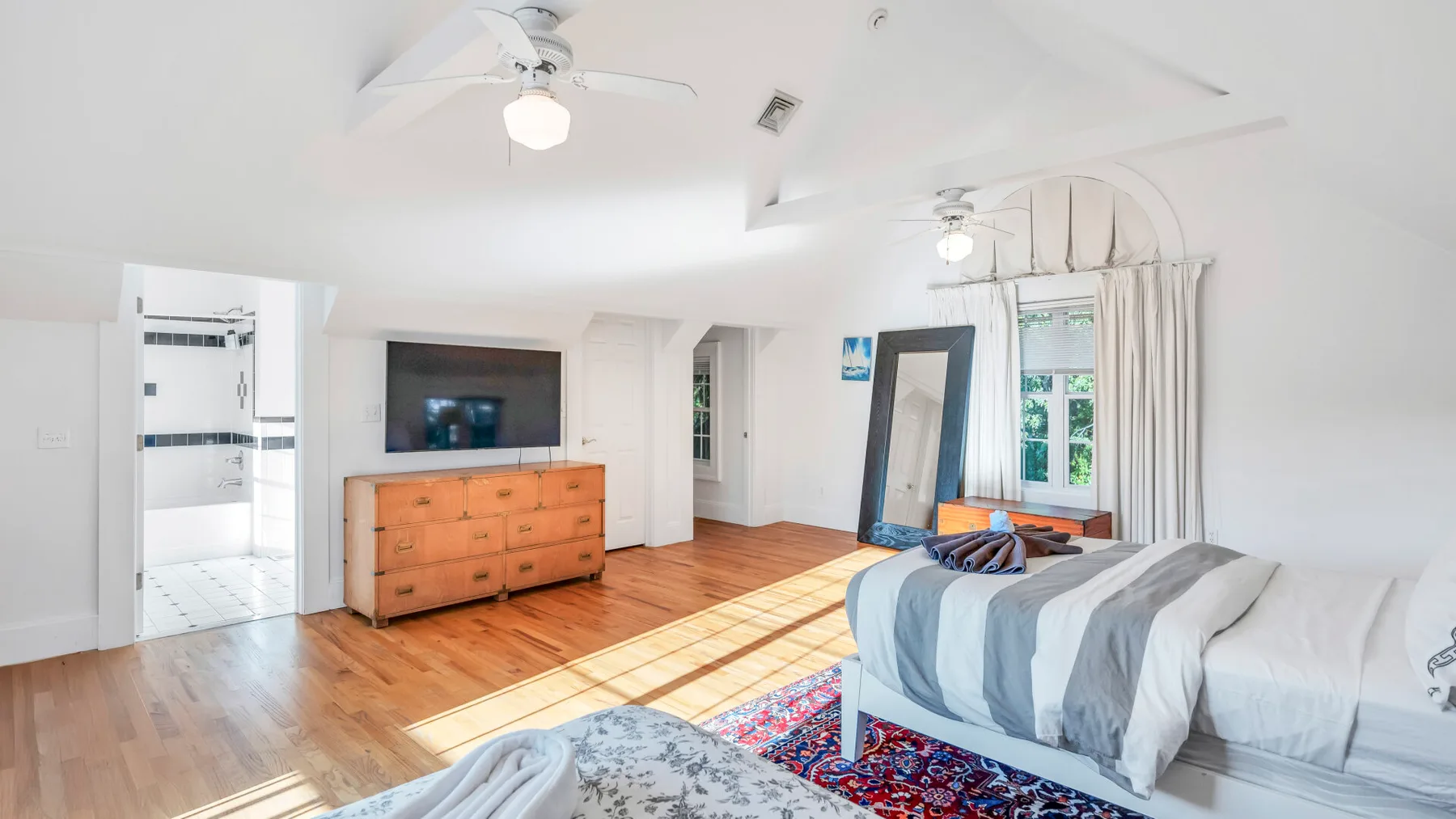 Un dormitorio luminoso con una cama, una cómoda de madera y luz solar en el suelo.