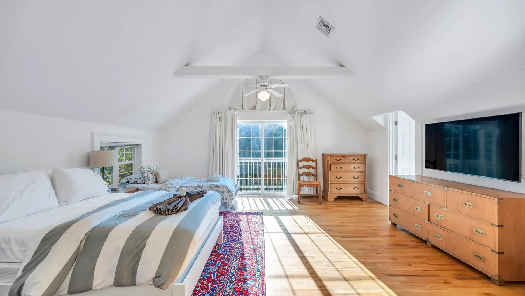 Un dormitorio luminoso con una cama, una cómoda de madera y un televisor grande.
