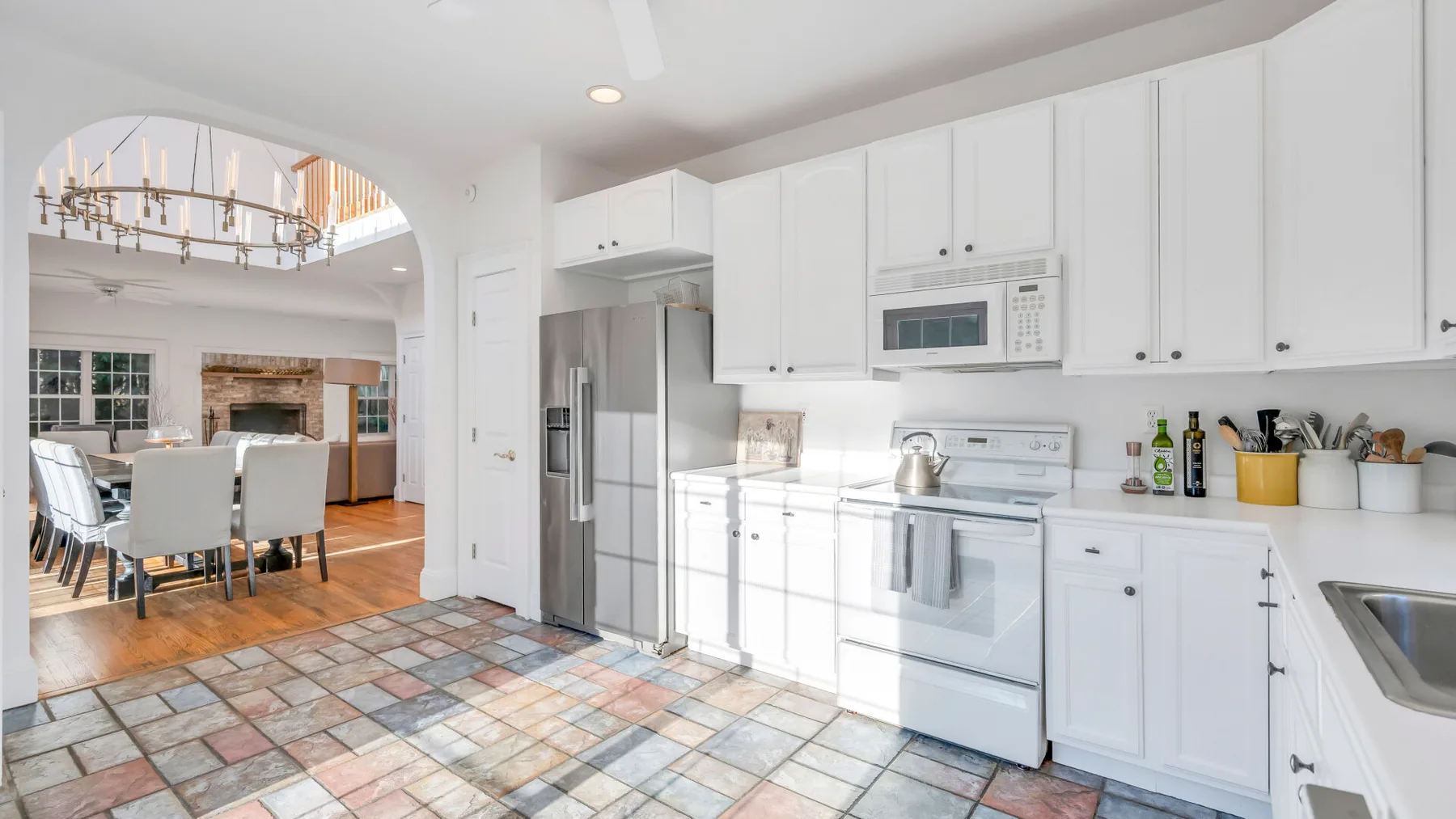 Una cocina blanca y luminosa con refrigerador de acero inoxidable y comedor contiguo.