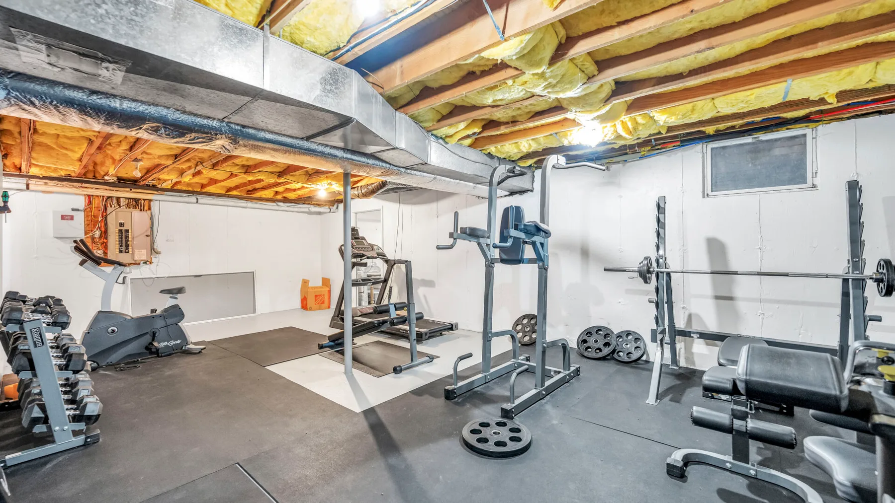 Un gimnasio en el sótano con máquinas de pesas, mancuernas y equipo de ejercicio.