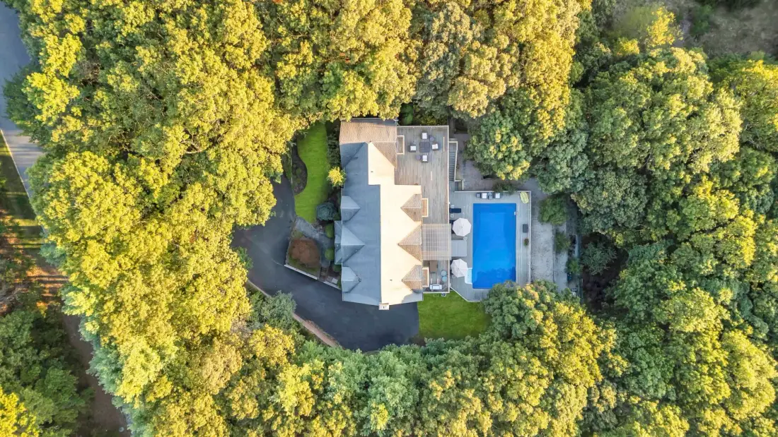 Una vista aérea muestra una casa y una piscina rodeadas de árboles frondosos.