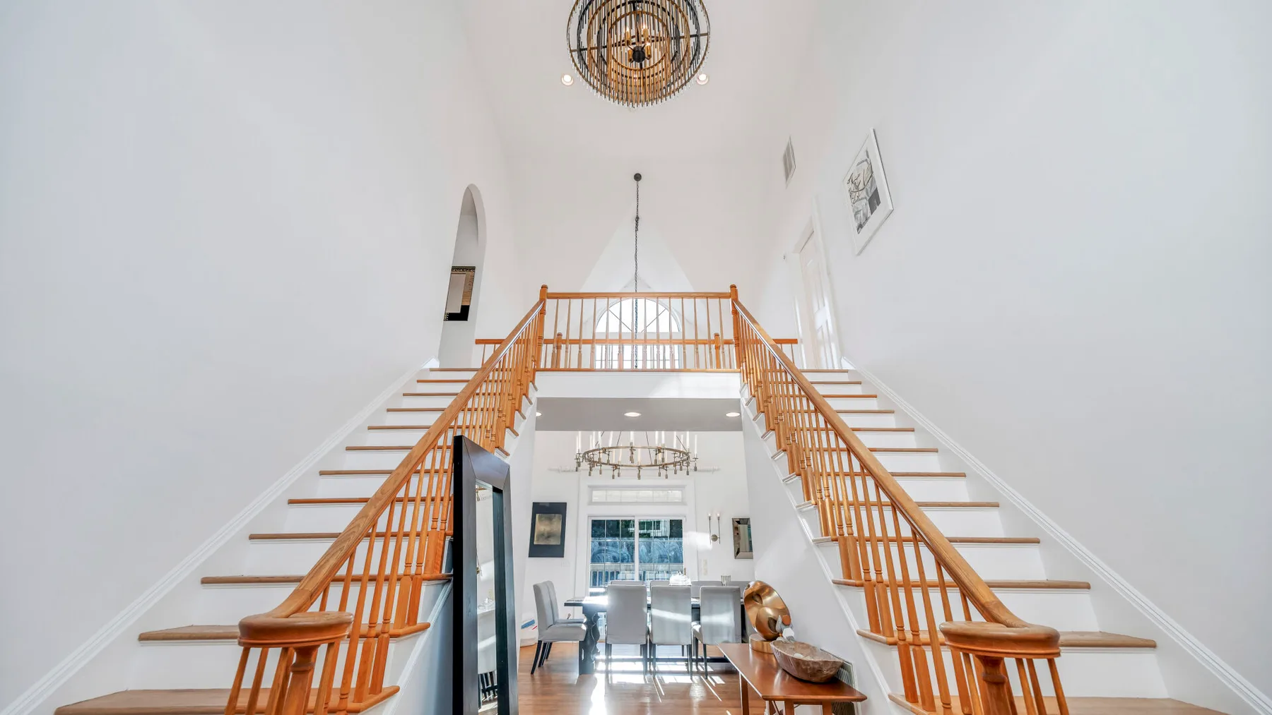 Un interior luminoso muestra una escalera dividida que conduce a un rellano sobre un comedor.