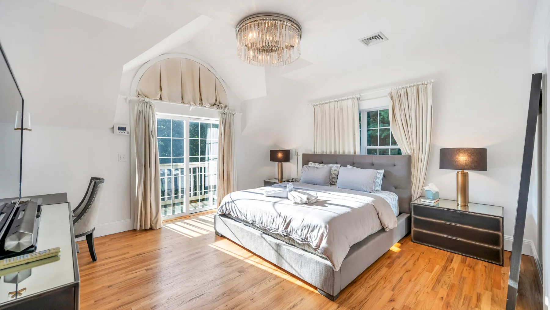 Un dormitorio luminoso con una cama grande, ventanas con cortinas y suelo de madera.