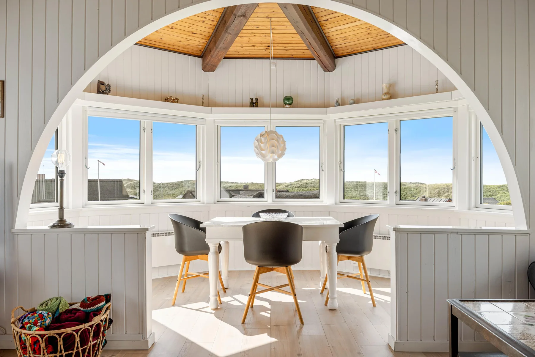 Un comedor con mesa y asientos está junto a grandes ventanas.