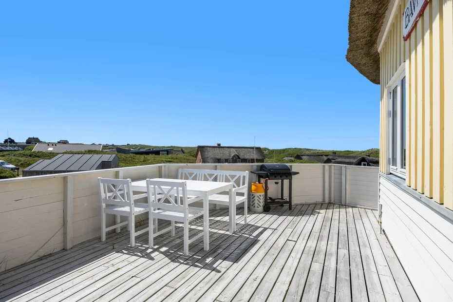 Una terraza en la azotea tiene asientos blancos al aire libre y vistas de los tejados cercanos.