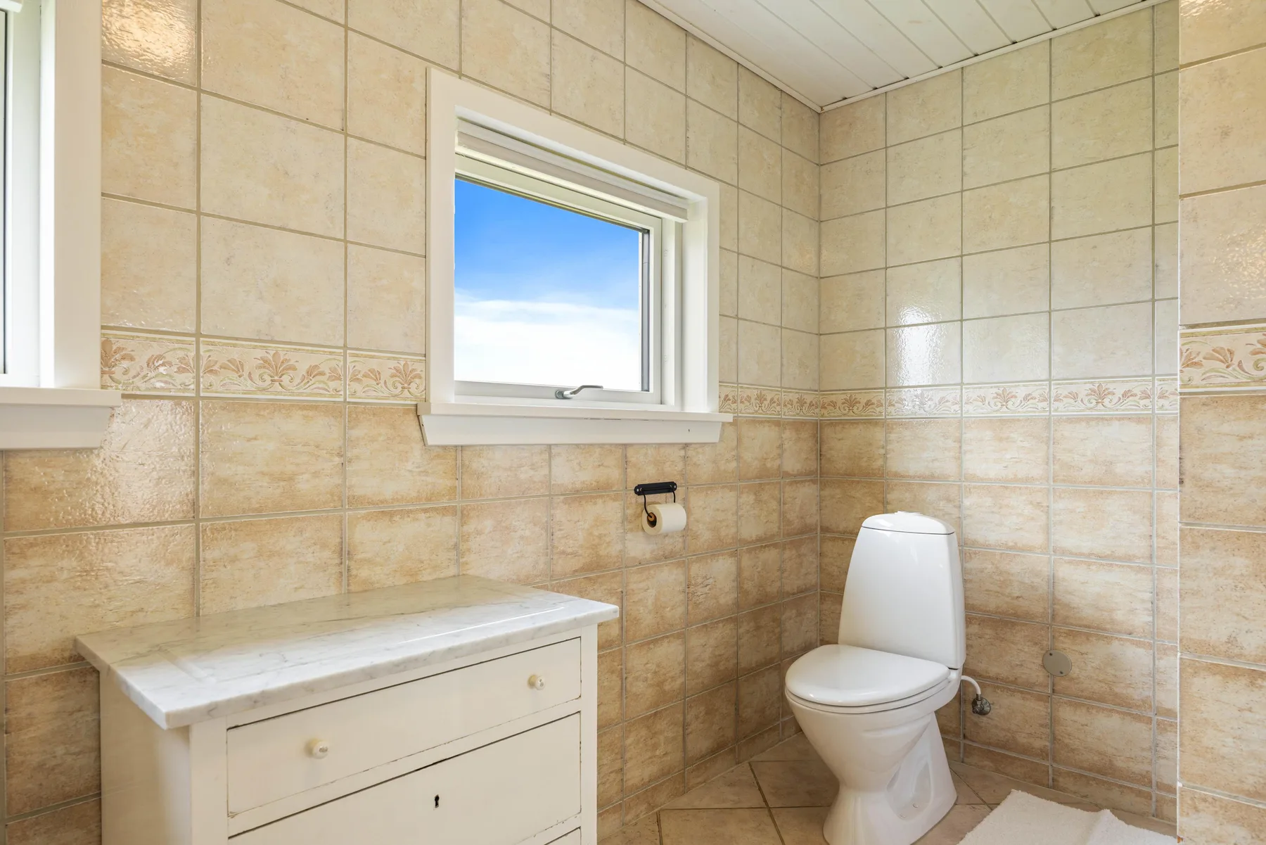 Un baño alicatado con inodoro, mueble de lavabo y ventana.