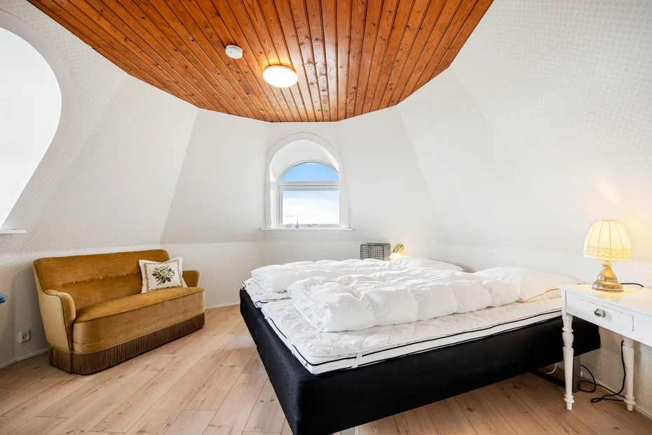 Un dormitorio luminoso con una cama, un techo de madera y una ventana pequeña.