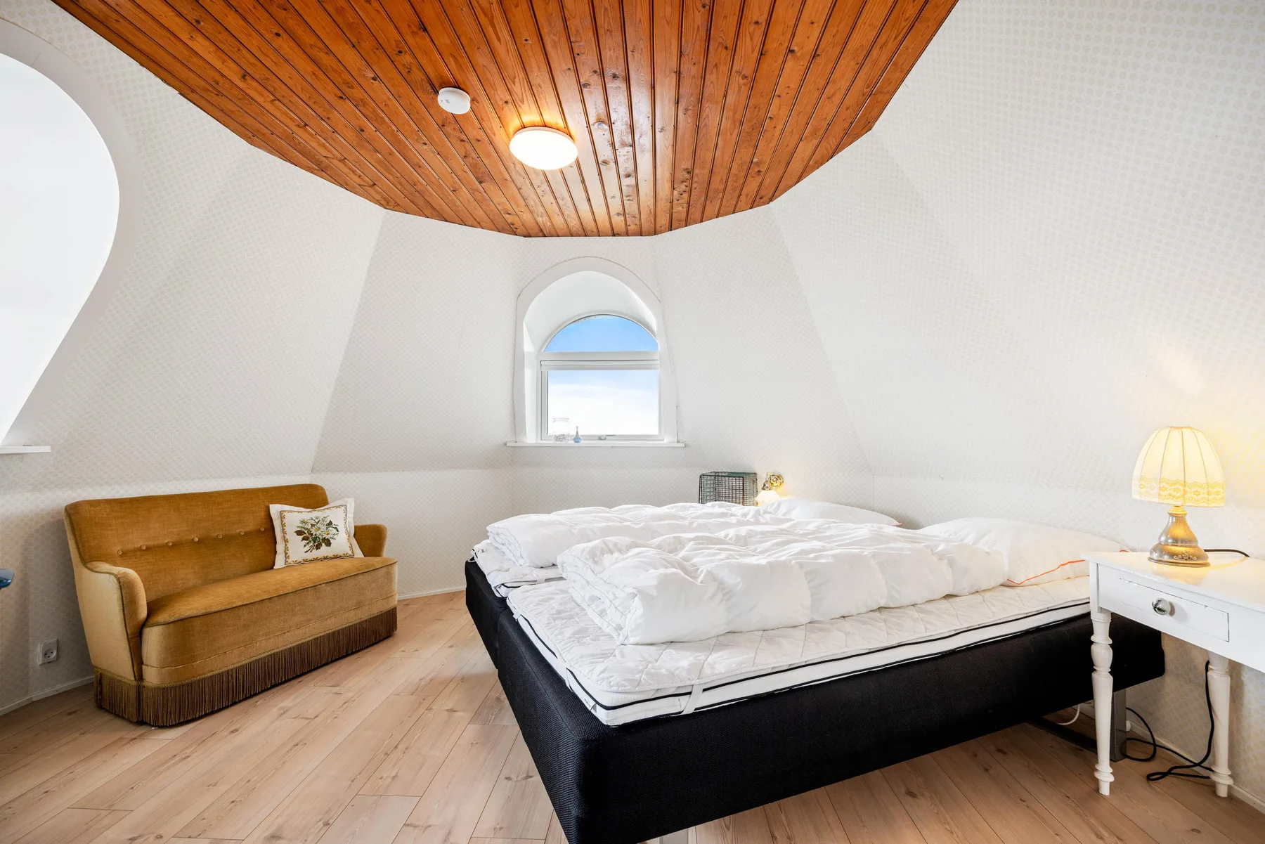 Dormitorio con una cama, una pequeña zona de estar y un techo inclinado de madera.