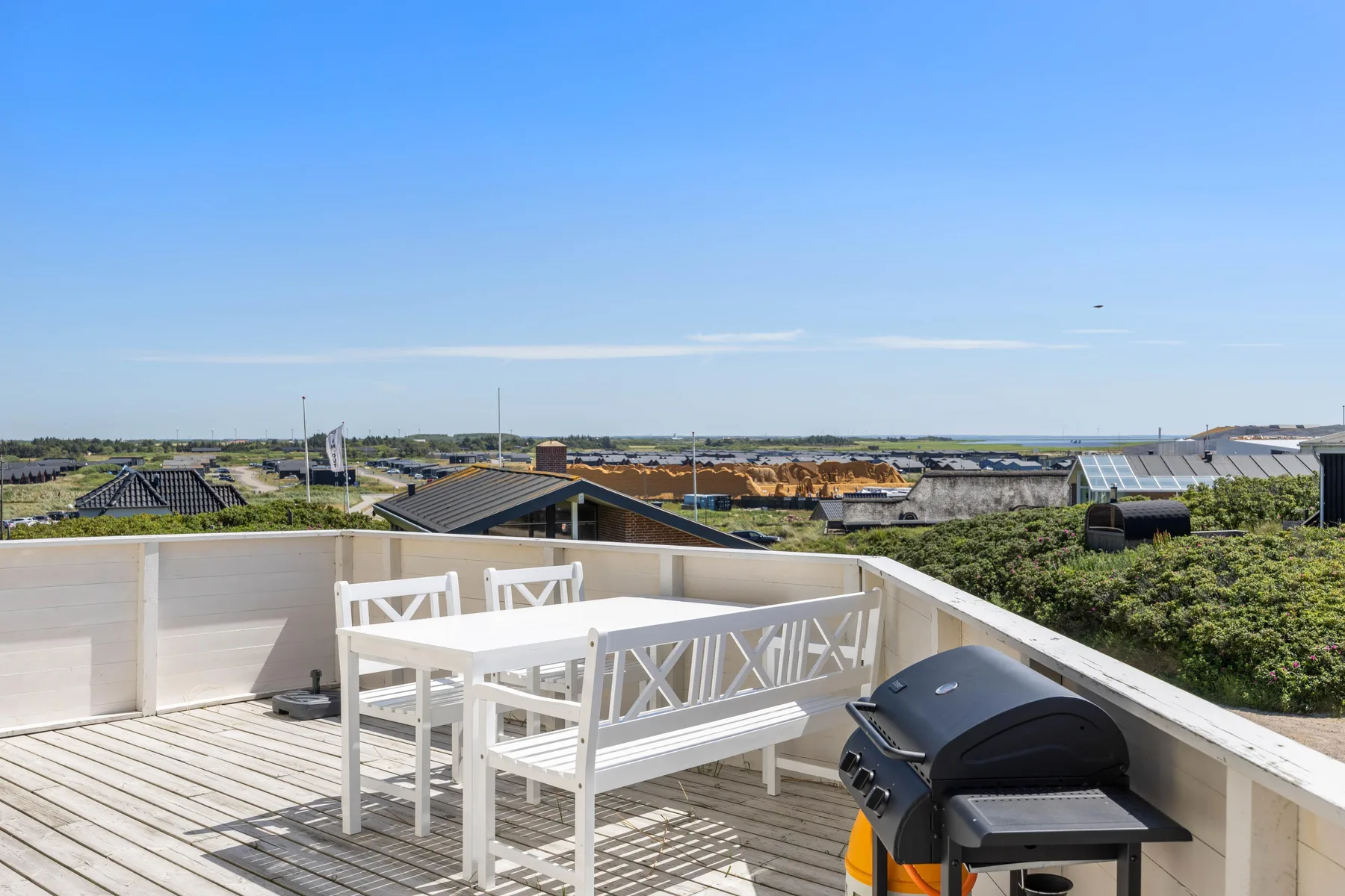 Una terraza en la azotea con asientos blancos y una parrilla da a los tejados cercanos.