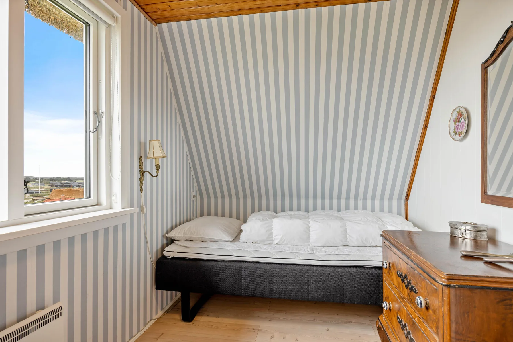 Un dormitorio con una cama bajo paredes a rayas y un techo inclinado.