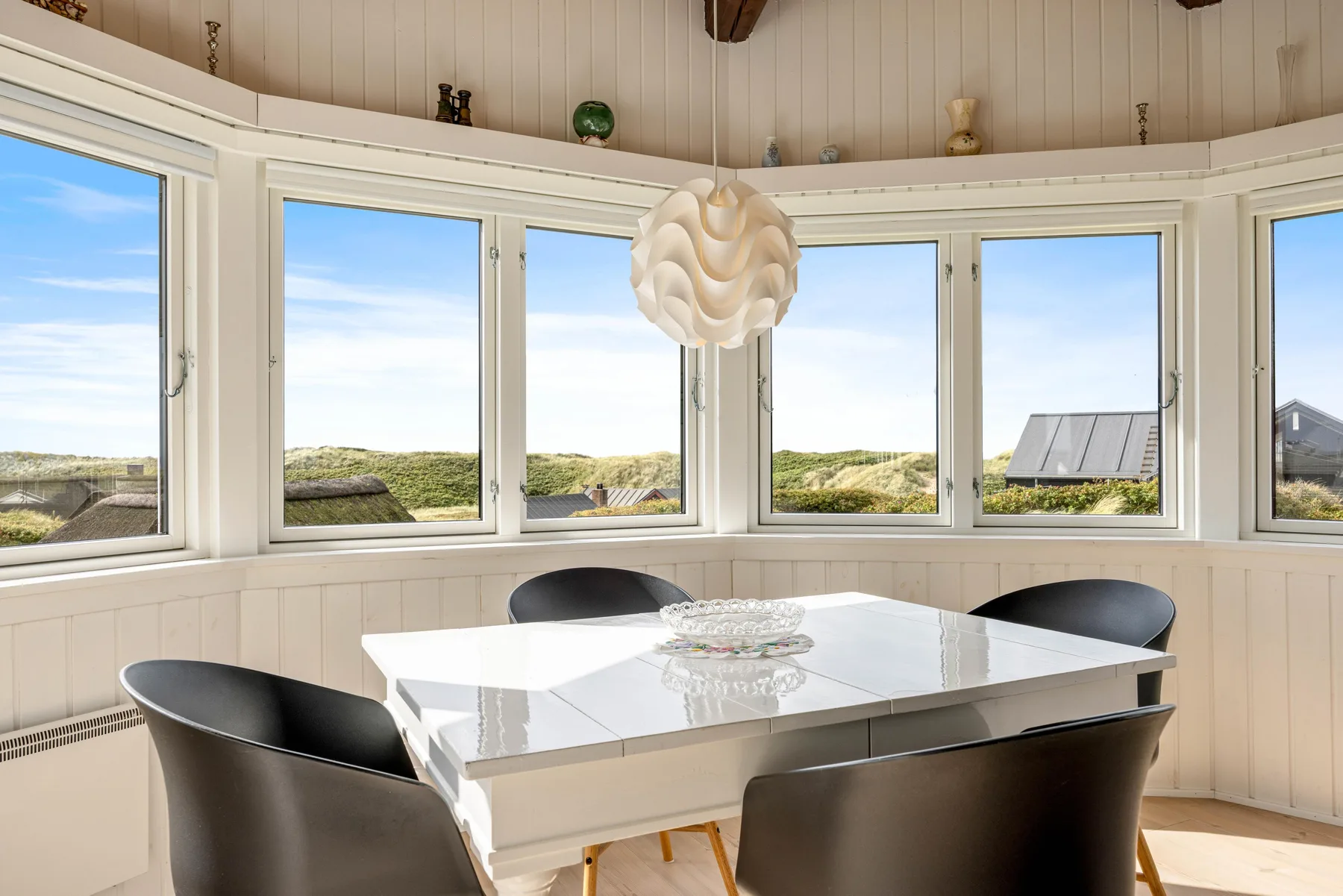 Comedor con una mesa y asientos junto a amplias ventanas con vistas al paisaje.