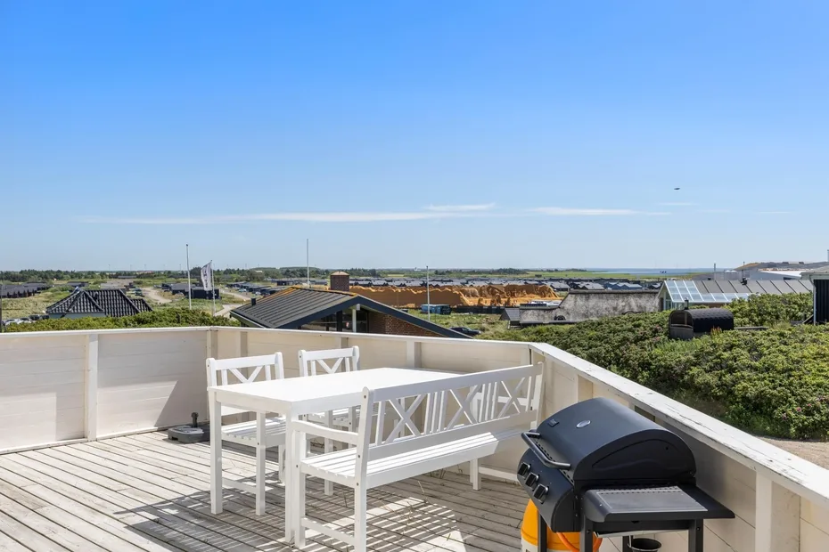 Una terraza en la azotea tiene asientos blancos al aire libre y una parrilla.