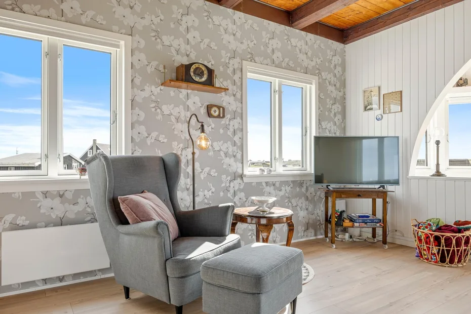 Una sala luminosa con un sillón gris junto a las ventanas.