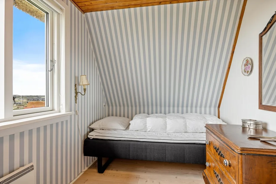 Un dormitorio con una cama bajo papel pintado a rayas y un techo de madera.