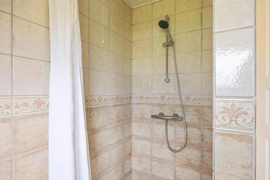 Una ducha alicatada con ducha de mano y cortina blanca.