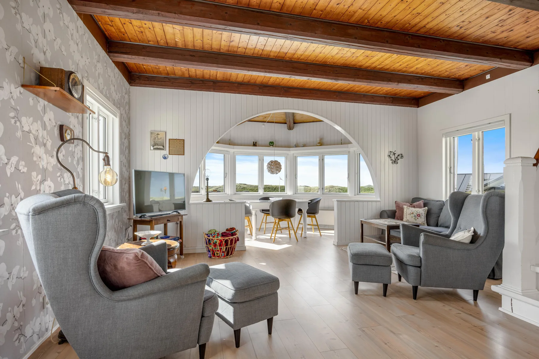 Una luminosa sala de estar con asientos grises y un comedor junto a las ventanas.