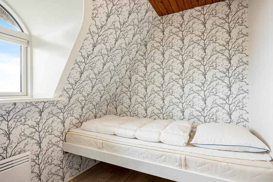 Una cama está junto a una pared cubierta de papel tapiz con ramas.