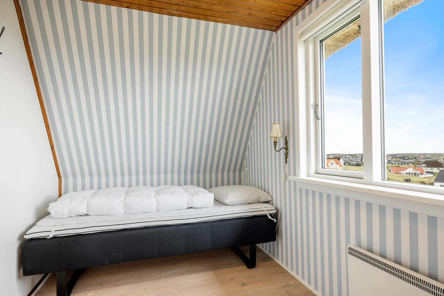 Dormitorio con una cama bajo paredes a rayas y una ventana.
