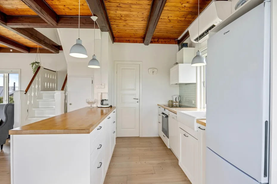 Una cocina luminosa con armarios blancos, una isla central y vigas de madera a la vista.