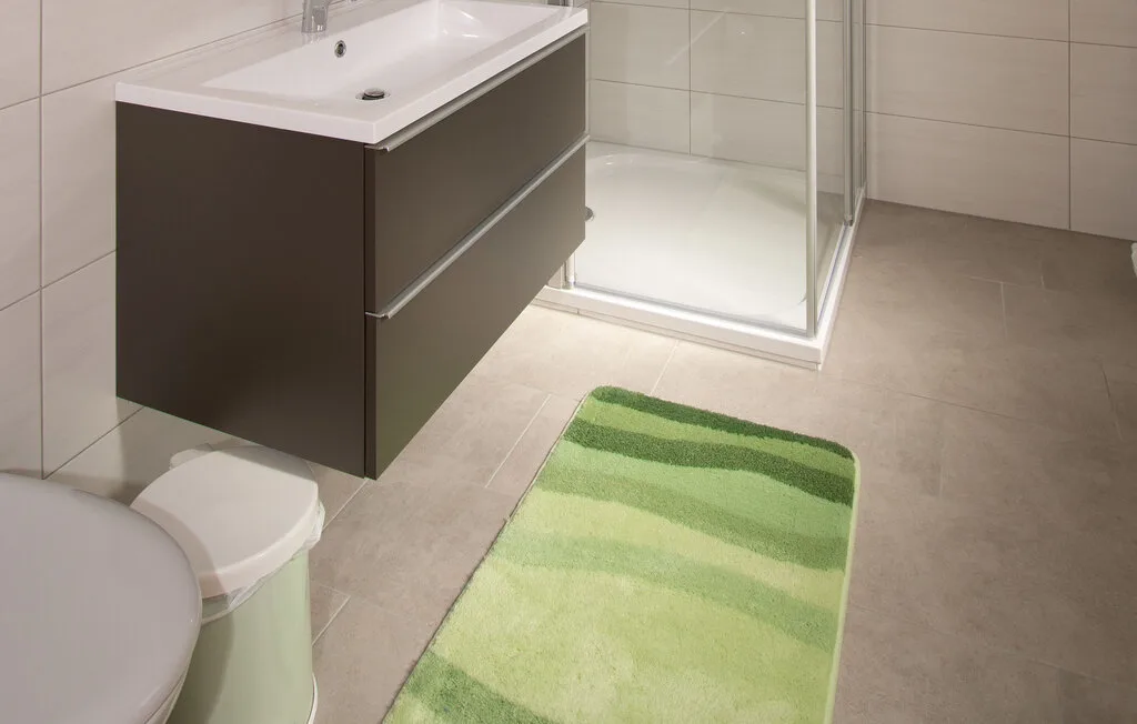 Un baño con lavabo, ducha y alfombra de baño verde.
