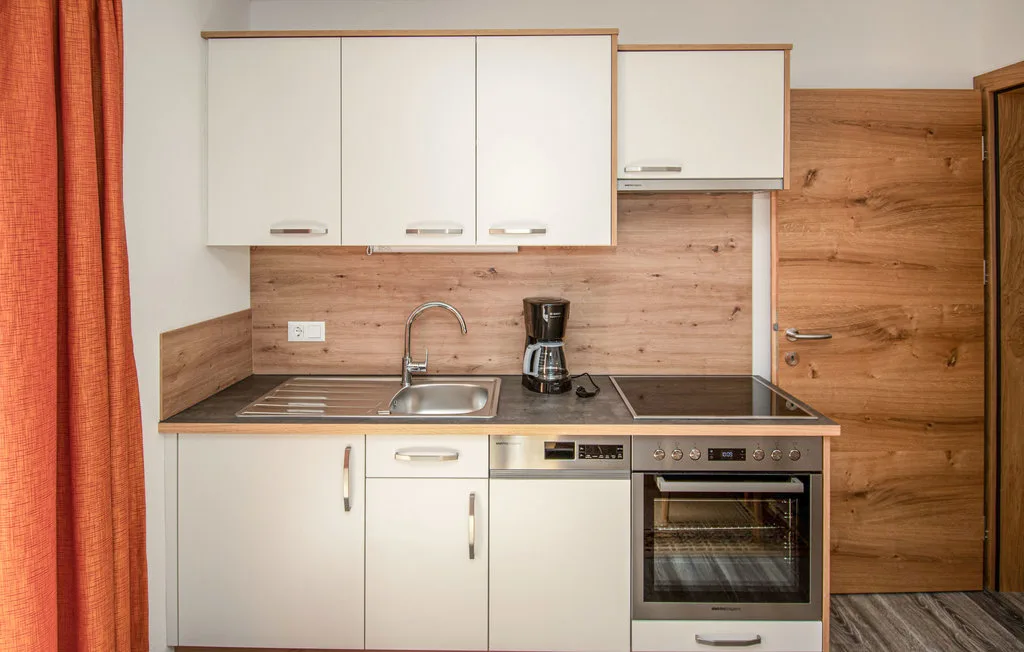 Una cocina compacta con armarios blancos, una encimera y un horno.