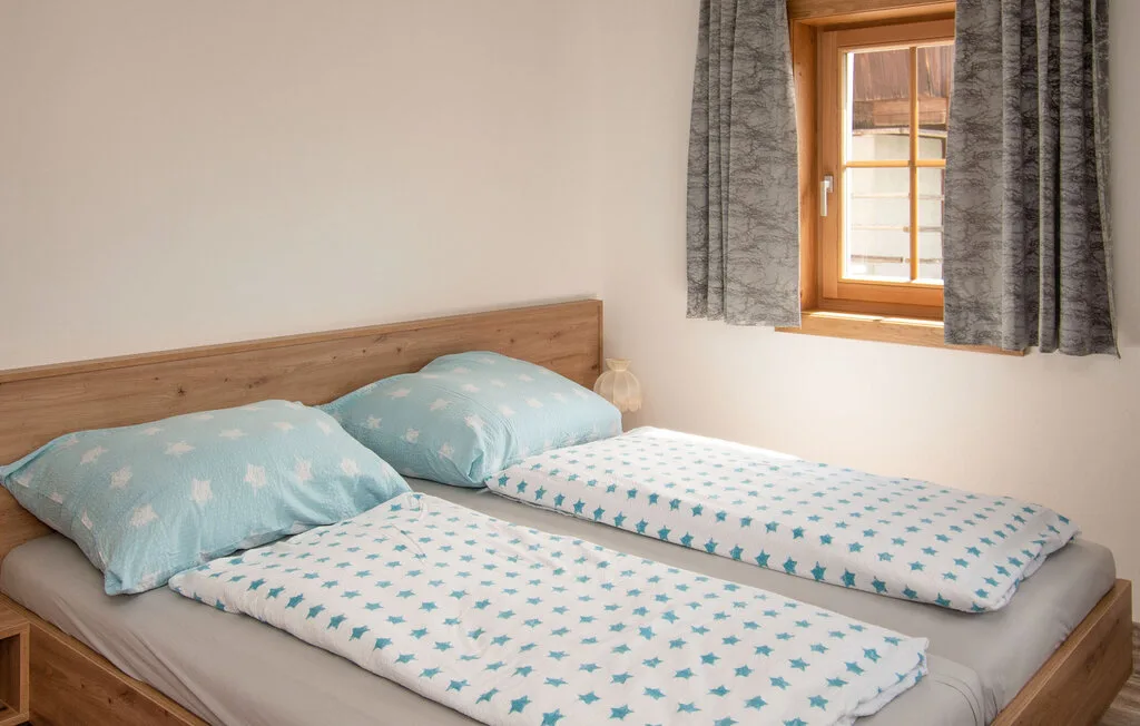 Un dormitorio con dos camas vestidas con ropa de cama azul claro estampada bajo una ventana con cortinas.