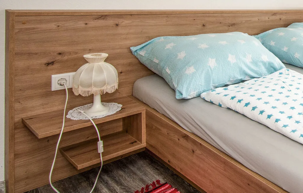 Un dormitorio con una repisa de madera junto a la cama y ropa de cama azul claro.