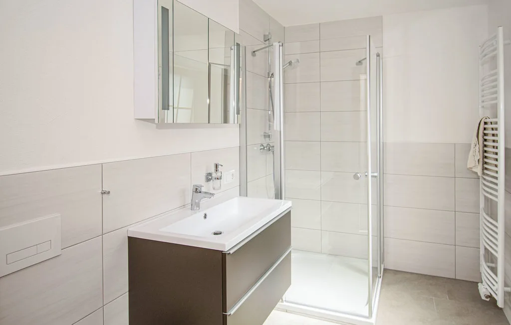 Un baño luminoso con lavabo, armario con espejo y ducha de cristal.